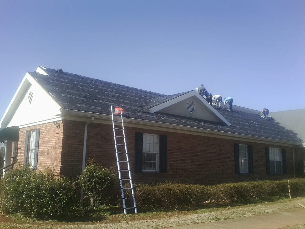 Crew tearing shingles off a brick ranch roof with a ladder set — Metal Roof Repair work by our crew in Ashley Falls