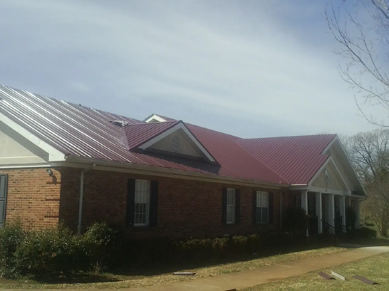 Red metal roof with gabled entries on a long brick building, from a Hail Damage Roof Repair job in Ashley Falls