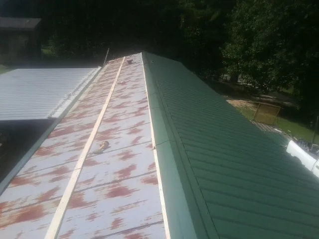 Old rusted panels beside newly installed green metal roofing — Wind Damage Roof Repair by Roofing Brothers in Ashley Falls
