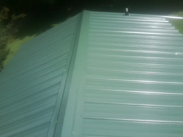 New green metal panels meeting at the ridge of a roof — Flat Roof Repair work by our crew in Ashley Falls