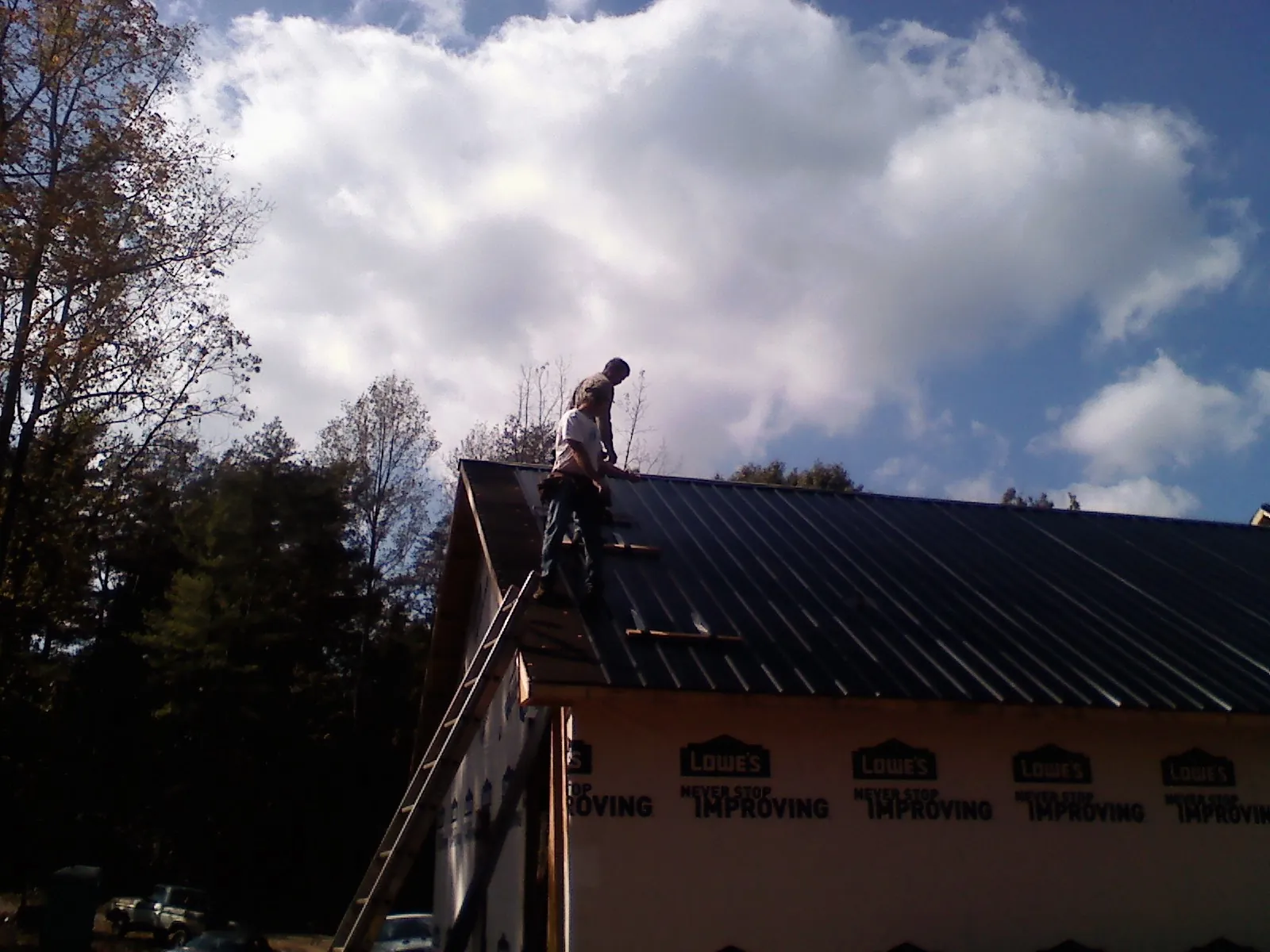 Roofer fastening dark metal panels high against a cloudy sky, from a Roof Inspection job in Ashley Falls