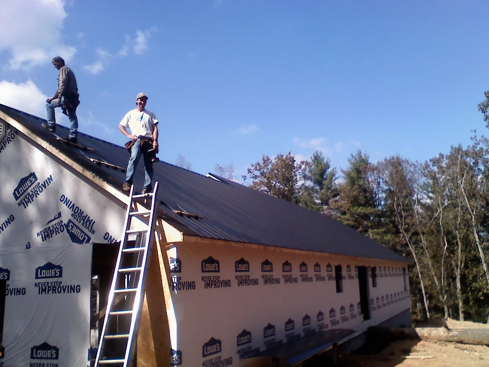 Two roofers standing on a long dark metal roof over a wrapped building in Ashley Falls