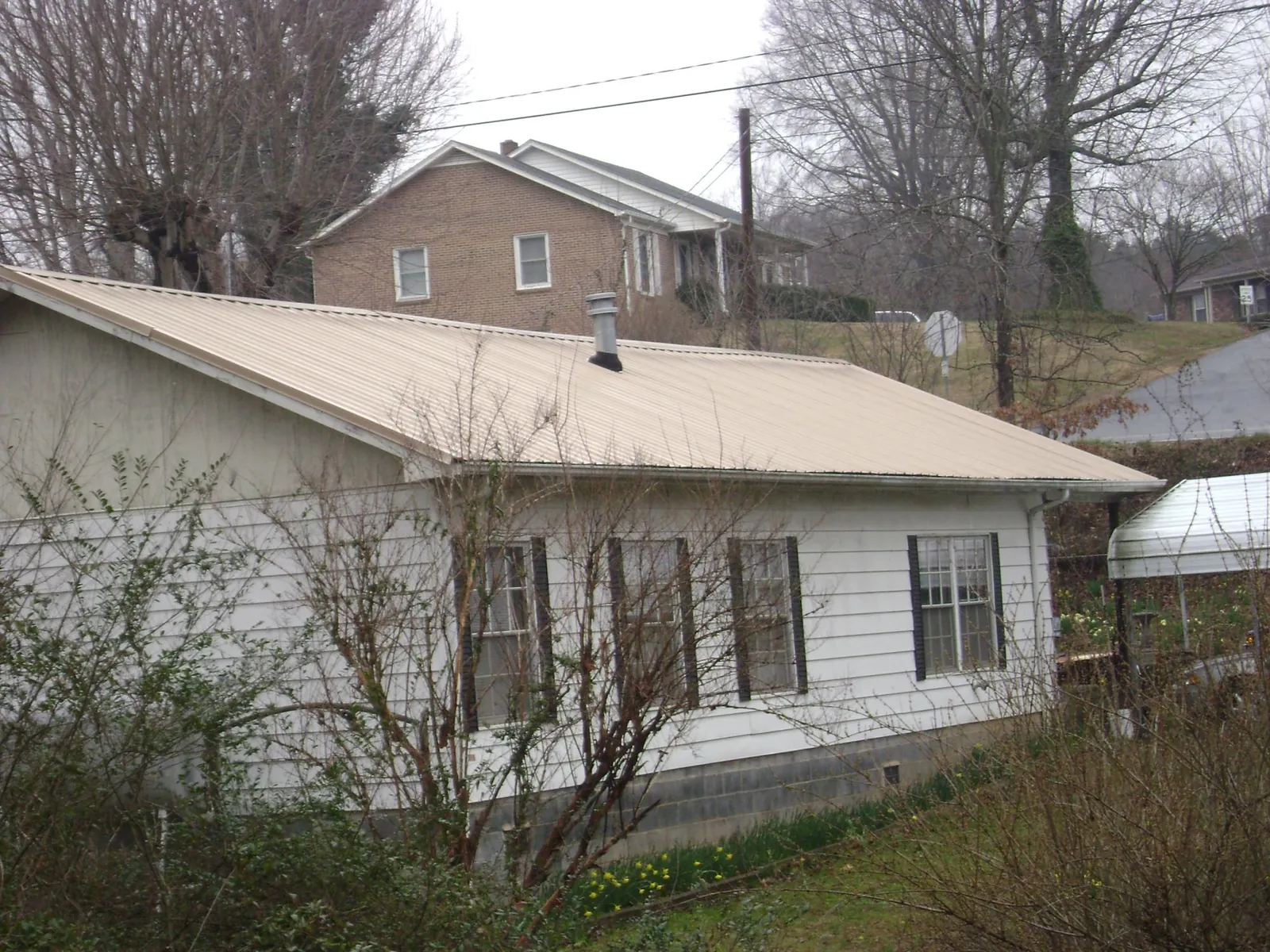 Tan metal roof on a white sided house set into a hillside — Commercial Roofing by Roofing Brothers in Ashley Falls