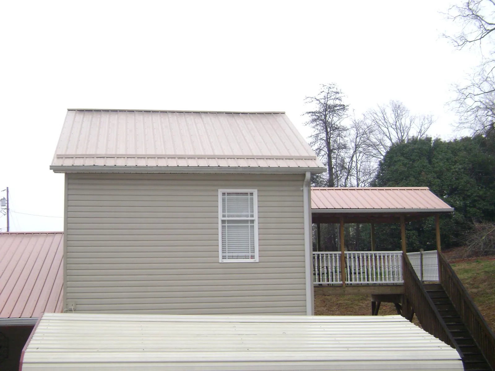 Tan metal roofs on a two story addition and attached porch, from a Roof Replacement job in Ashley Falls